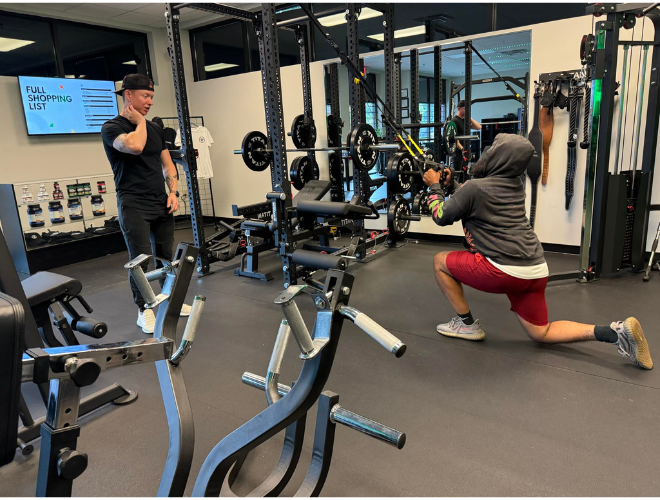 A personal trainer coaching a client performing a lunge exercise in a modern gym.